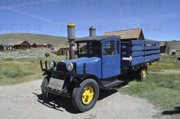 A blue historic truck with yellow wheels, Dodge Graham 1927, stands in front of a wooden house village in rural surroundings, Bodie Ghost Town, California, USA