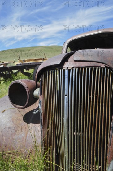 Close-up of a rusty car wreck, Chevrolet Coupé, against blue sky and green area, Bodie Ghost Town, California, USA
