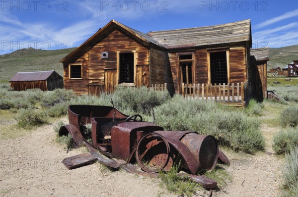 Old wooden house with rusty car wreck in front of it, surrounded by nature, Bodie Ghost Town, California, USA