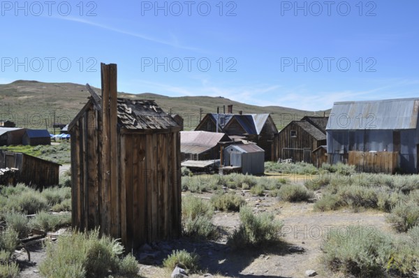 An abandoned village with several wooden houses, toilet, outhouse in the foreground, in a natural, rural area, Bodie ghost town, California, USA
