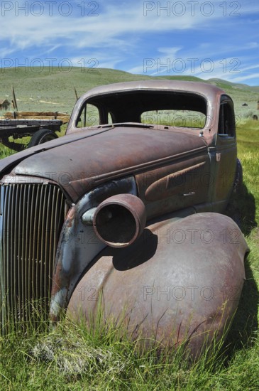Front view of abandoned rusty car wreck, Chevrolet Coupé, under blue sky, Bodie Ghost Town, California, USA