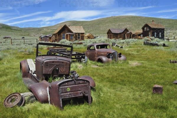 Rusty vehicles, car wrecks, on green area with old abandoned houses, Bodie Ghost Town, California, USA