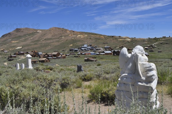 Angel statue in a cemetery overlooking a ghost town in the distance, Bodie Ghost Town, California, USA