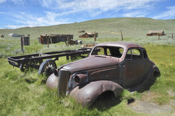 Rusty car wreck, Chevrolet Coupé, in front of historic buildings in natural setting, Bodie Ghost Town, California, USA