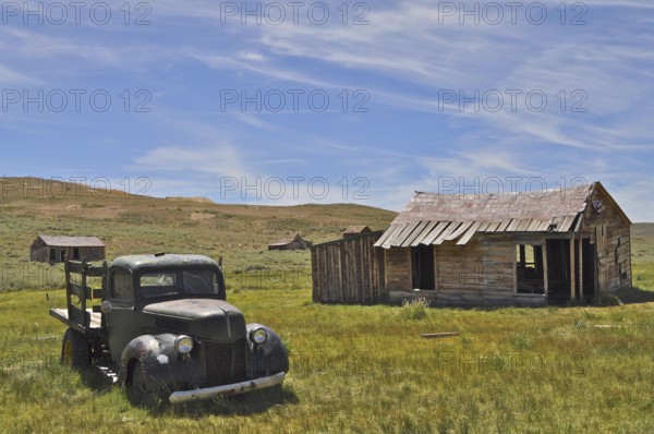 An abandoned car, vintage Ford Model 51 pickup truck, stands next to an old wooden cabin in a barren, rural landscape, Bodie Ghost Town, California, USA