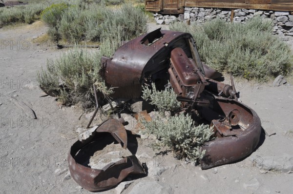Old crumbling car wreck in a dry landscape with plants, Bodie Ghost Town, California, USA