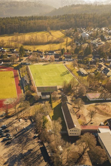 Residential area with sports ground and lots of trees in sunlight taken from the air, Wimberg, Calw, Germany