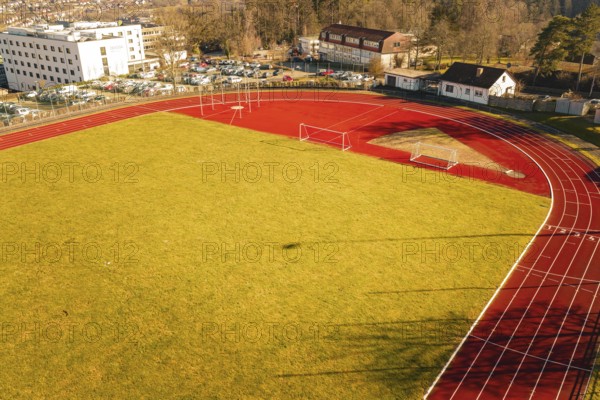 Aerial view of a sports field with red running track, yellow lawn and surrounding buildings, Wimberg, Calw, Germany