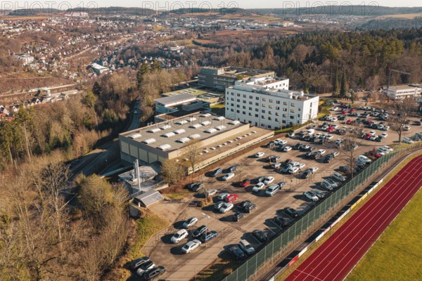 School with parking lot and several cars in a winter landscape with city and hills in the background, Wimberg, Calw, Germany