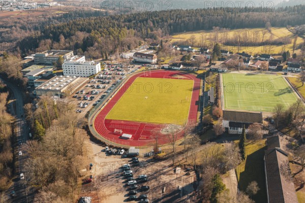 Aerial view of a sports complex with red running track and surrounding village and forest, Wimberg, Calw, Germany