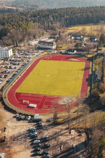 Red track with green grass and surrounding forest in a village, seen from the air, Wimberg, Calw, Germany
