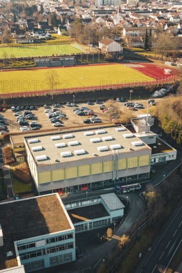 Overview of a sports field with parking lot and school complex in urban and natural surroundings in winter, Wimberg, Calw, Germany