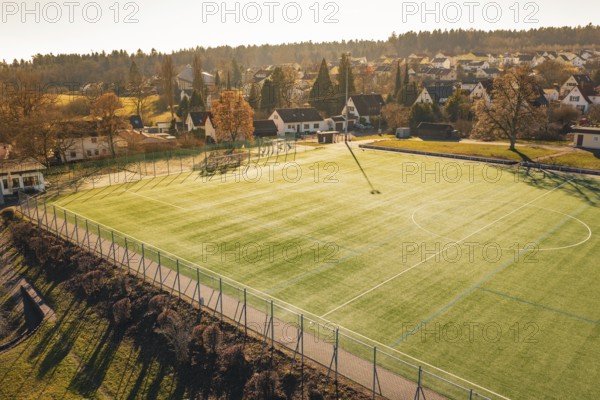 Football field is illuminated by sunlight, surrounded by village houses and trees, Wimberg, Calw, Germany