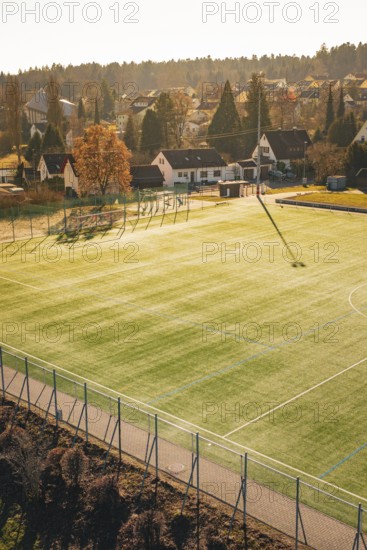 Sunlight illuminates a soccer field in the village with houses and trees in the background, Wimberg, Calw, Germany