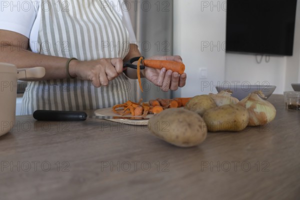 Close up of hands peeling fresh carrot in home kitchen. Healthy ingredients, simple food preparation and everyday cooking concept