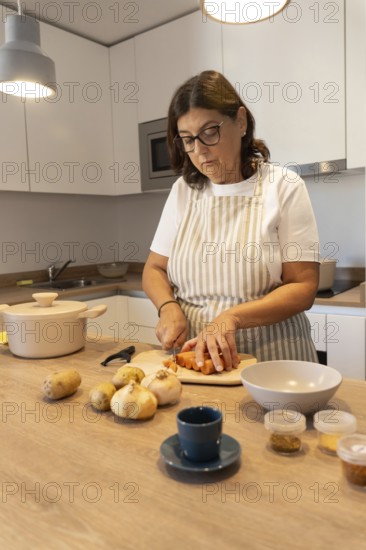 Middle aged woman cooking at home, cutting vegetables on wooden countertop. Simple ingredients, cozy kitchen atmosphere, everyday routine and nutritious homemade food concept