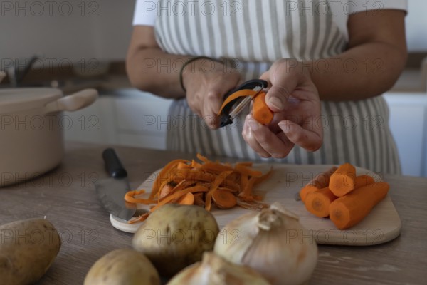 Hands peeling carrots while preparing vegetables at home. Casual lifestyle, healthy ingredients and cozy kitchen environment