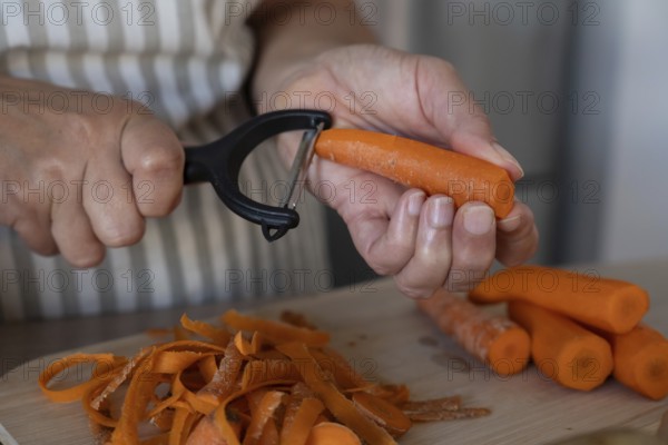 Close up of hands peeling fresh carrot on cutting board in modern kitchen. Simple ingredients, healthy cooking and everyday food preparation