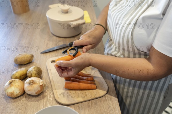 Woman peeling carrots for soup preparation in kitchen. Comfort food, homemade cooking and healthy nutrition concept