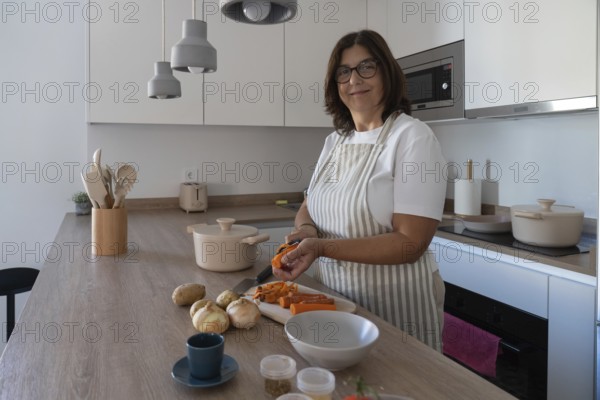 Woman preparing carrots, potatoes and onion for homemade soup in modern kitchen. Comfort food, simple ingredients and healthy cooking concept