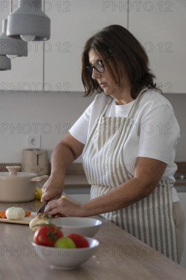 Woman chopping onion on kitchen counter with selective focus on woman. Food preparation and everyday home cooking scene