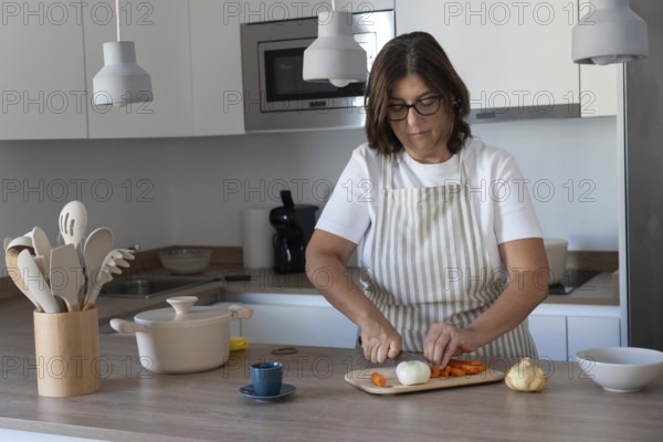 Cozy home kitchen scene with woman wearing apron cutting carrots and preparing vegetables. Comfort food and healthy lifestyle concept