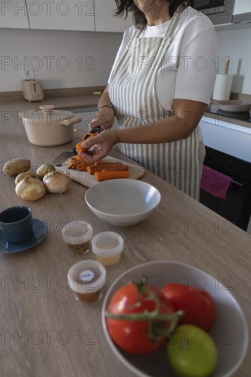 Vertical close up of hands peeling fresh carrot on cutting board in modern kitchen. Healthy cooking, simple ingredients and everyday home lifestyle with copy space