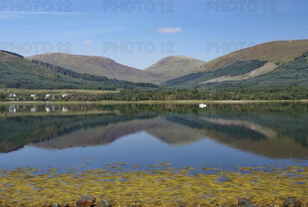 A calm body of water reflects the surrounding mountains and clear skies, Highlands, Fort William, Scotland, Great Britain