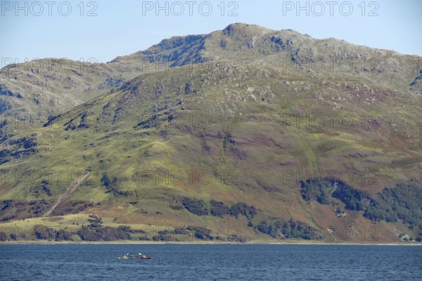 Mountain backdrop with calm lake and canoeists under clear sky, Knoydart, Mallaig, Scotland, Great Britain