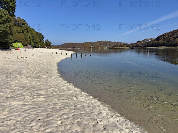 Quiet sandy beach with water views and wooded hills, Silver Sands of Morar, Mallaig, Scotland, United Kingdom