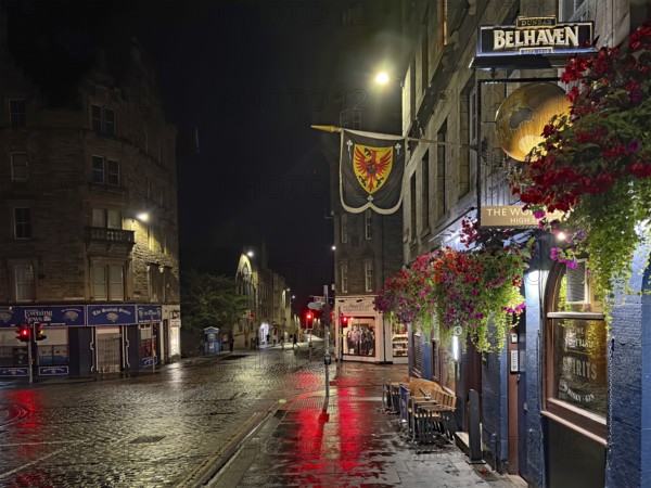 Night view of a quiet city street with wet pavement and illuminated shops. Royal Mile, Edinburgh, Scotland, United Kingdom