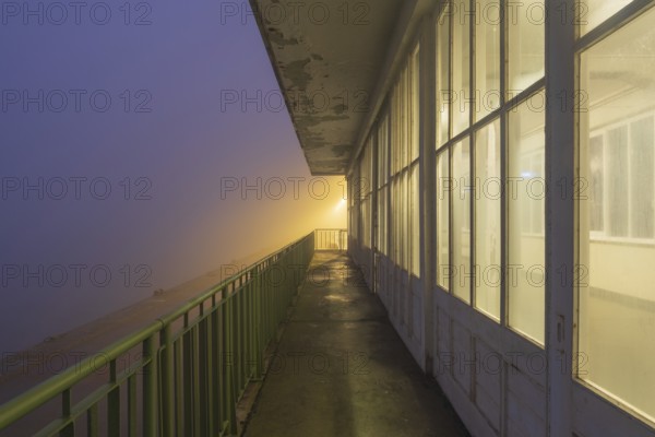 View along a long balcony of Steubenhöft at night in fog, Cuxhaven, Lower Saxony, Germany