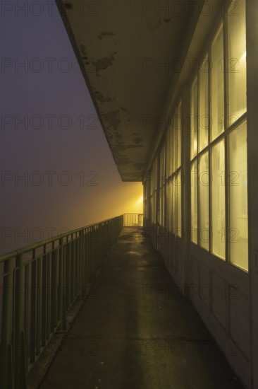 View along a long balcony of Steubenhöft at night in fog, Cuxhaven, Lower Saxony, Germany