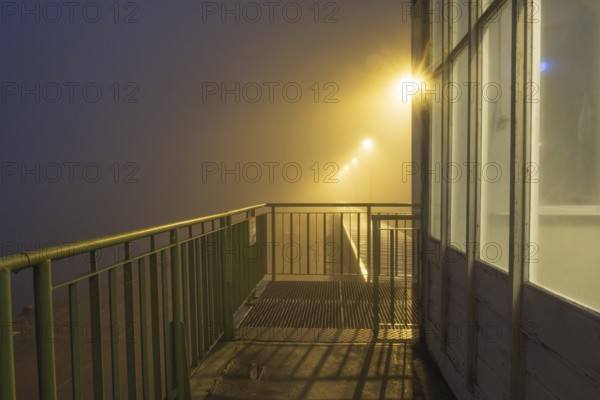 View along a balcony of Steubenhöft at night in fog, Cuxhaven, Lower Saxony, Germany