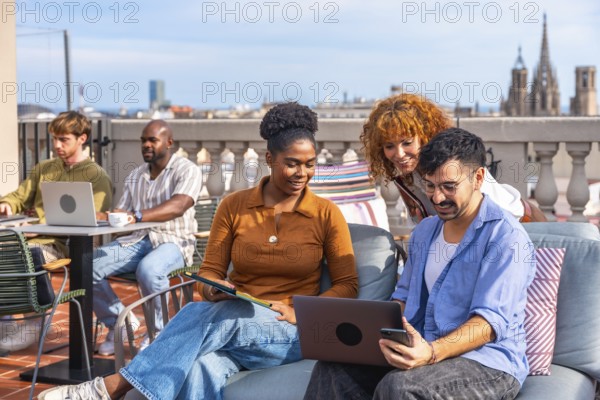 Diverse young professionals collaborating on a modern rooftop terrace, using laptops and smartphones to brainstorm, plan and connect in a casual, creative urban work setting