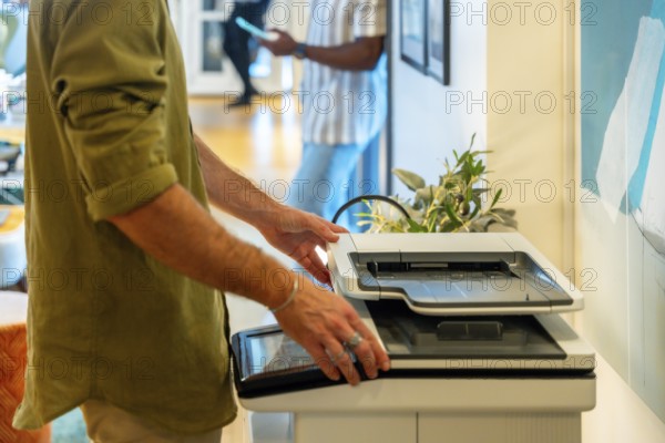 Coworker standing near a multifunction printer, opening the scanner lid to place a document for scanning, highlighting office technology and daily tasks in a shared workspace