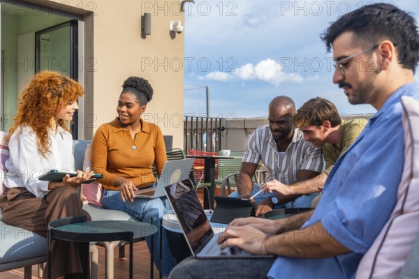 Group of diverse business people using laptops and tablets while working together on a collaborative project during a casual meeting on an urban rooftop office