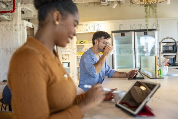 Coworkers are enjoying a coffee break in a modern co working space, using tablets for work or leisure, fostering a contemporary and flexible work environment