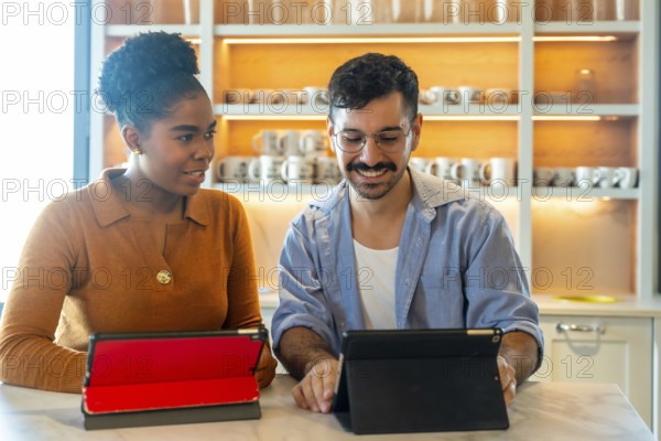 Diverse business colleagues collaborating and reviewing content on digital tablets during a break, discussing ideas in a comfortable coworking kitchen area