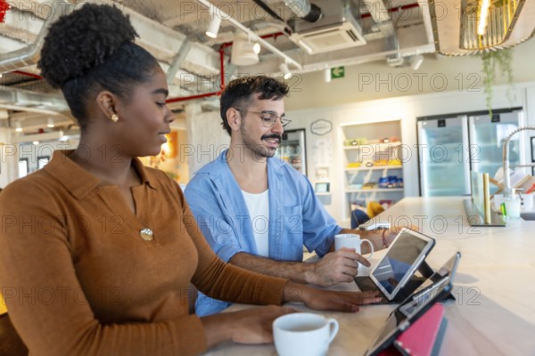 Diverse colleagues in a modern office breakroom are collaborating and discussing work using digital tablets while enjoying coffee, representing teamwork, technology, and a productive environment