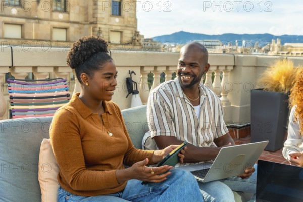 Two diverse colleagues working together and discussing ideas during a casual rooftop meeting, collaborating outdoors on a sunny day with city buildings in the background