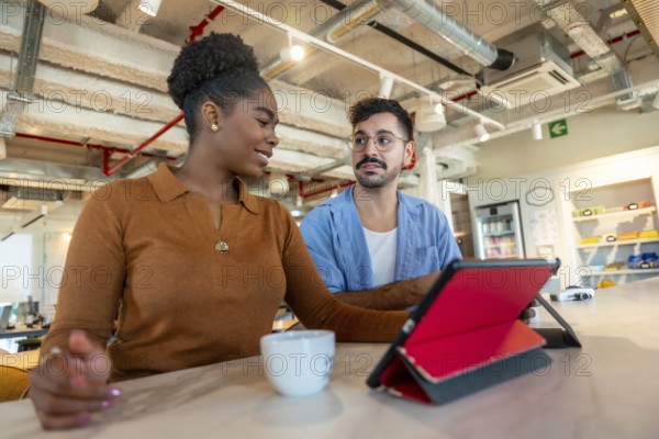 Diverse colleagues collaborate during a working break in a modern coworking office, discussing ideas and planning work while utilizing a digital tablet