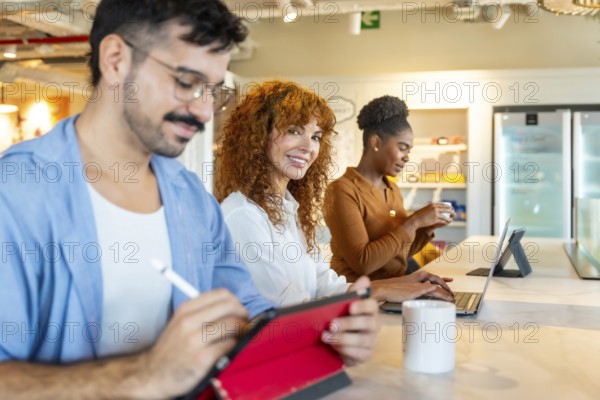 Group of diverse business professionals using digital devices and interacting during a break in a contemporary shared office, fostering teamwork, innovation, and a dynamic work environment