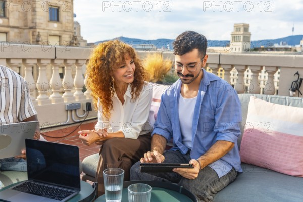 Two diverse colleagues collaborating during an outdoor business meeting on a professional coworking rooftop, using a laptop and tablet for teamwork and planning