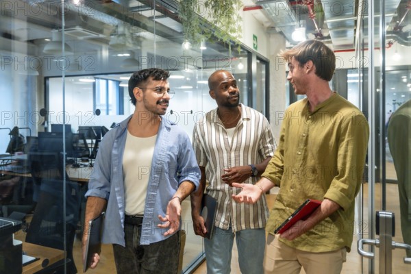 Diverse group of male colleagues engaging in a friendly discussion while walking through a modern coworking office space, fostering teamwork and collaboration