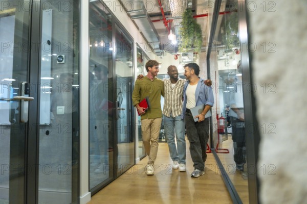 Three smiling diverse colleagues walking together embraced through a modern office building hallway, sharing a moment of friendship and teamwork during their work break