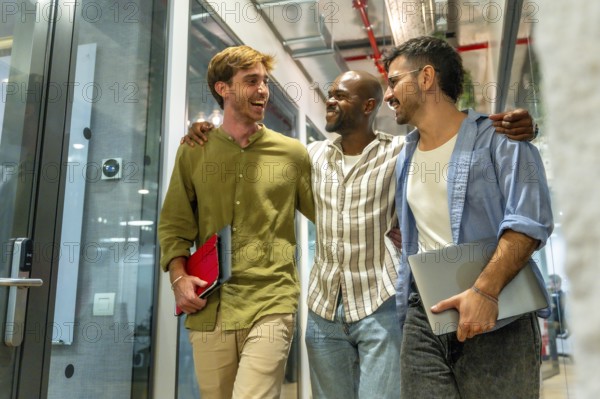 Diverse group of men colleagues walking through a modern office building, laughing and smiling while carrying laptops and folders, symbolizing teamwork and positive workplace collaboration