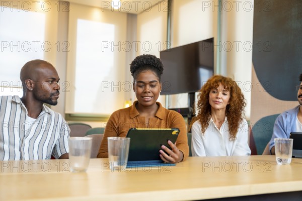 Diverse business colleagues are engaging in a collaborative meeting, discussing ideas and working together in a modern office or coworking space, with one person using a digital tablet