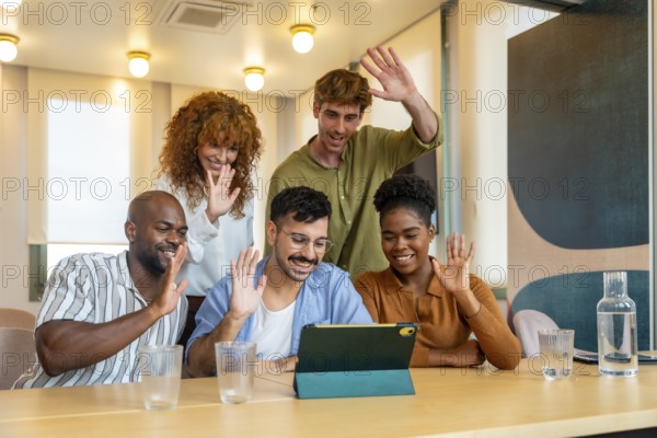 Group of diverse colleagues waving to a tablet during a business video conference in a modern office, showing teamwork, communication, and connectivity