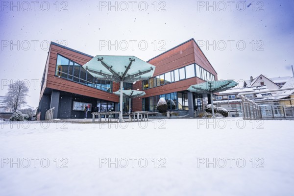 Modern town hall building with glass windows in winter surrounded by snow and cloudy sky, Gechingen, Calw district, Germany